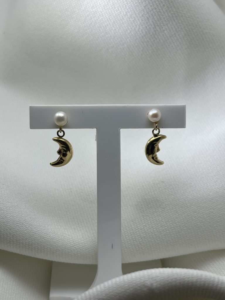 Boucles d'oreilles pendantes en or jaune 750, composées d'une perle de culture blanche et d'un croissant de lune ciselé d'un visage de profil. Un modèle délicat et poétique, à porter au quotidien