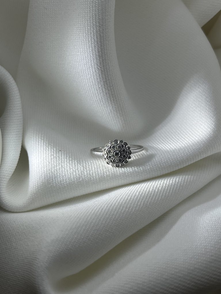 Une bague florale en or blanc 18 carats, construite autour d'une pierre centrale sertie clos et de deux entourages successifs. Un dessin d'inspiration rétro, lumineux sans être imposant.