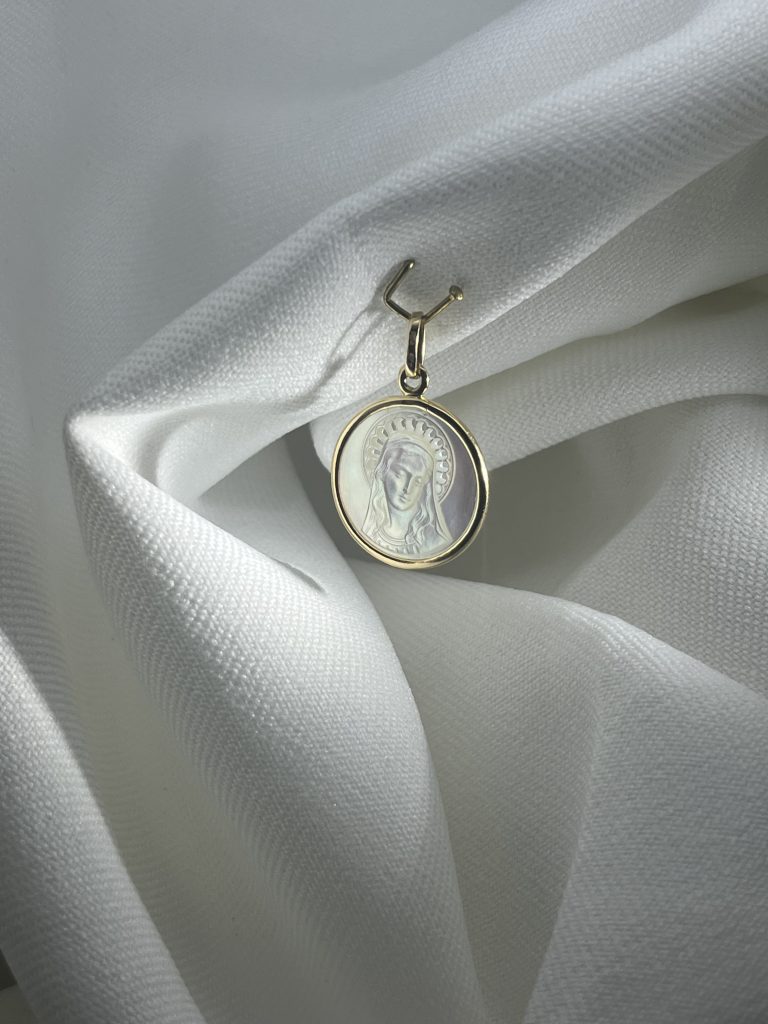 Médaille de la Vierge en nacre gravée, cerclée d'or jaune 18 carats, avec bélière en or, posée sur un drapé de tissu blanc.