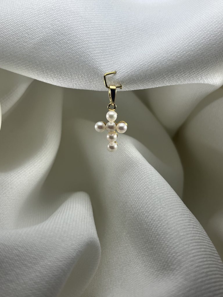 Croix en or jaune 18 carats sertie de six perles d'eau douce blanches, avec bélière en or, posée sur un drapé de tissu blanc.